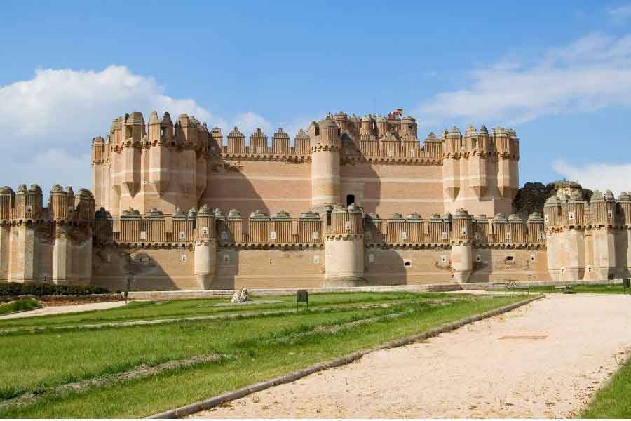 Castillo de Coca in Segovia province, a striking Mudejar-style fortress built with brick and decorated battlements, blending Gothic and Islamic design influences.