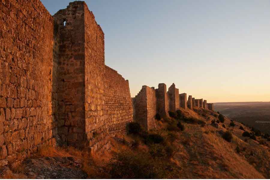 Castillo de Gormaz in Soria, the largest fortress of its kind in Europe, standing along a hilltop at sunset with ancient stone walls stretching into the distance.
