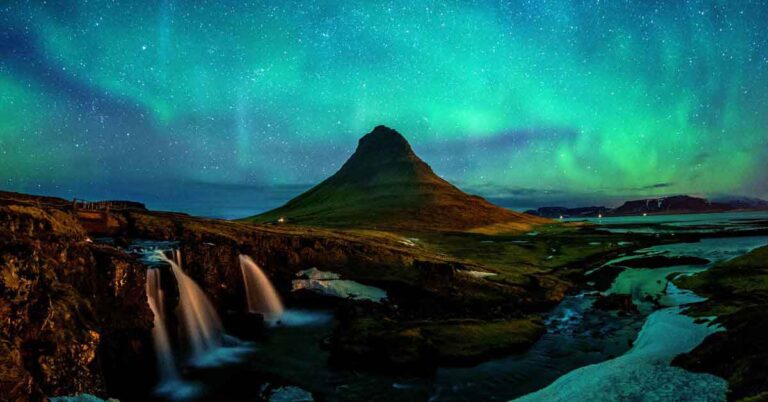 Dream travel destinations like Iceland’s Kirkjufell mountain under the glowing Northern Lights, with a cascading waterfall and a clear night sky filled with stars