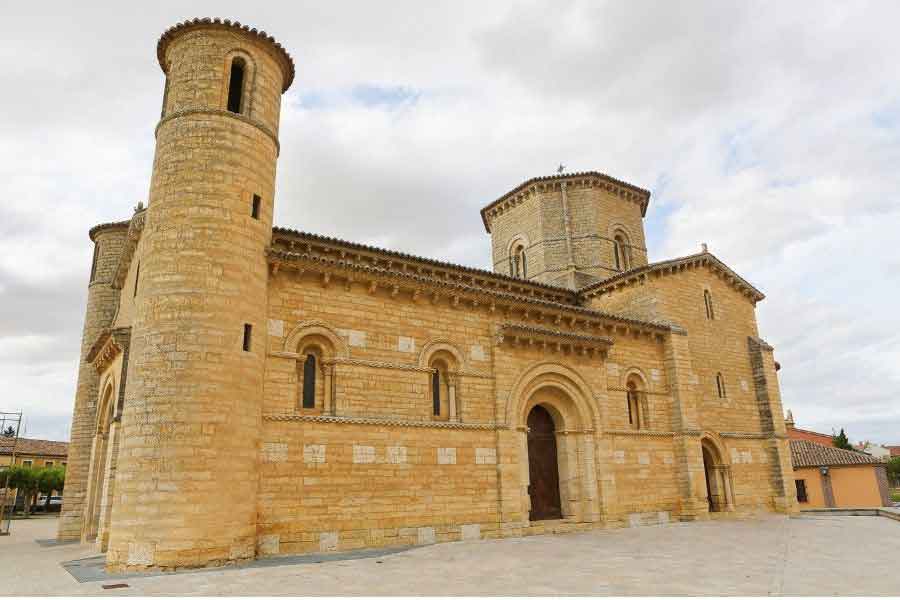 Iglesia de San Martín de Tours in Frómista, a Romanesque church in northern Spain with rounded towers, arched doorways, and light sandstone walls under a cloudy sky.