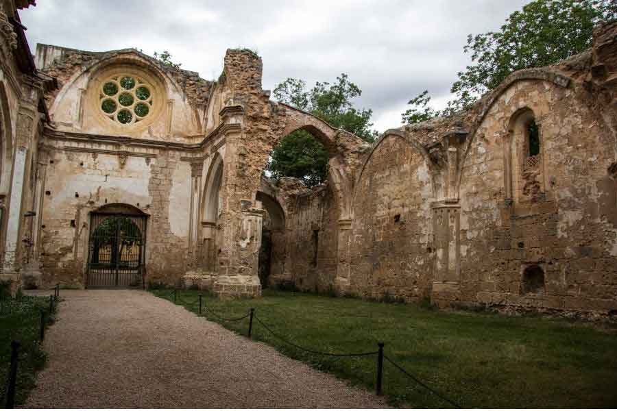 Ruins of the Monasterio de Piedra in Aragón, with crumbling stone arches and a rose window, surrounded by lush greenery in a peaceful natural setting.