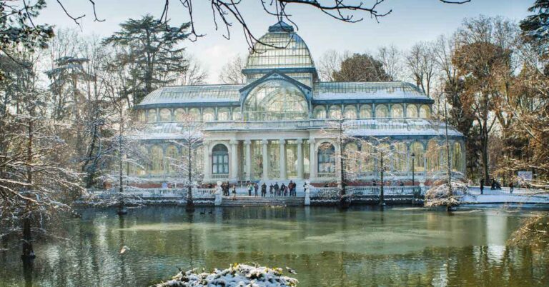 What to wear in Spain in winter — visitors walking around Madrid’s Palacio de Cristal surrounded by snow-covered trees, dressed warmly in coats, scarves, and hats for the cold season.