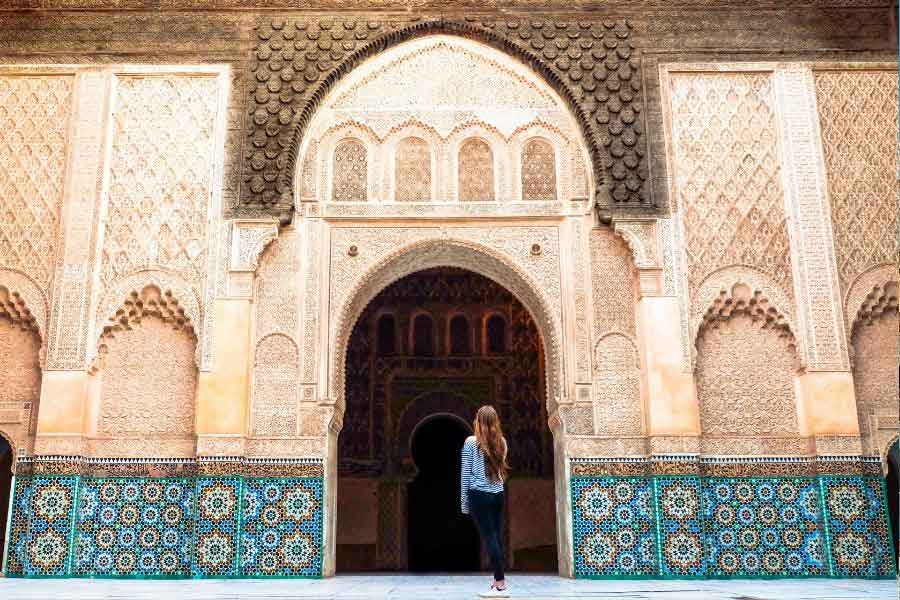 Sightseeing in Morocco in December A woman wearing modest layers and long trousers while visiting an ornate Moroccan building, showing what to wear in Morocco in winter.