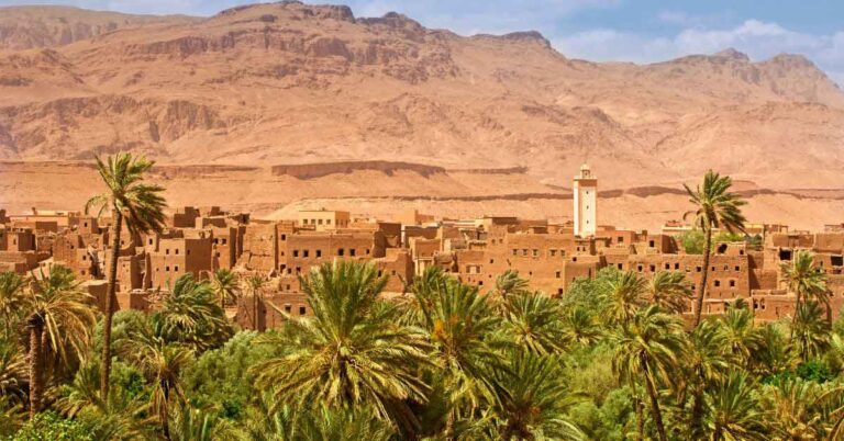 View of a traditional Moroccan village surrounded by palm trees and desert mountains under a clear sky — a beautiful reason to visit Morocco in winter for warm weather and scenic landscapes.