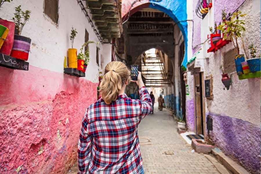Winter in Morocco A woman in a warm flannel shirt walking through a colourful Moroccan alley, showing a practical layering option for what to wear in Morocco in winter and how to dress for cooler winter days in Morocco.