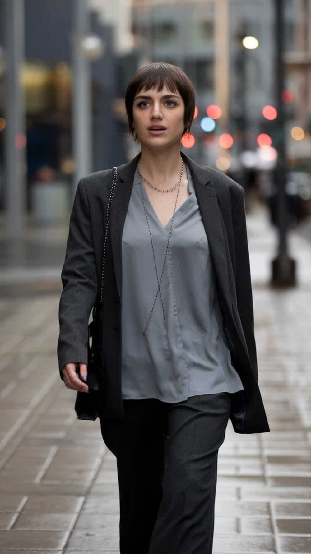 A person walking confidently in the city, sporting a pixie haircut with long bangs, dressed in a stylish outfit.