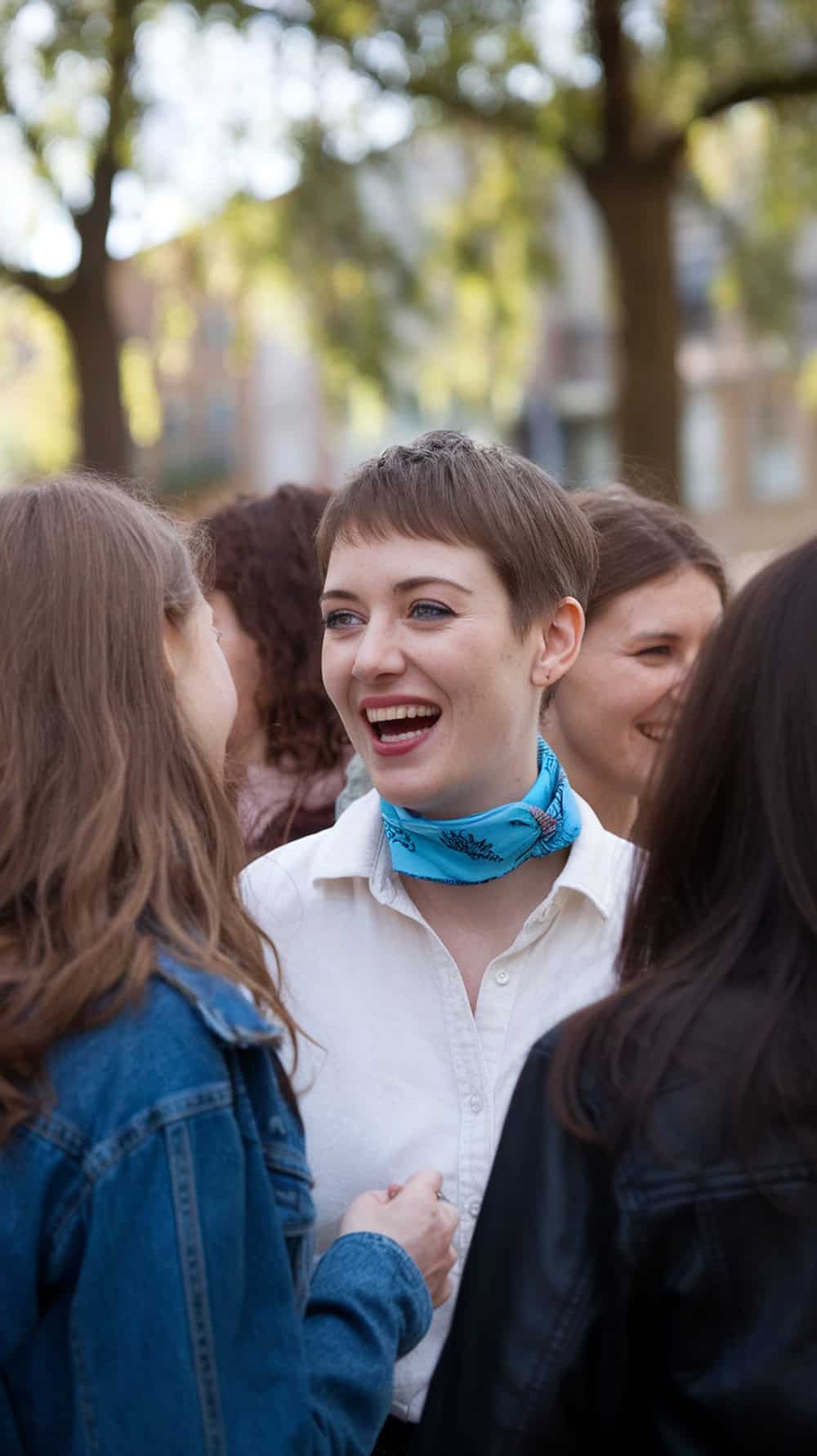A woman with a short pixie haircut, smiling and chatting with friends outdoors.