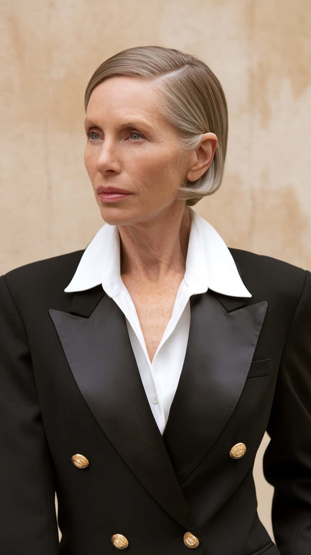 A woman with polished short hair styled in a center part, wearing a black blazer with a white shirt.