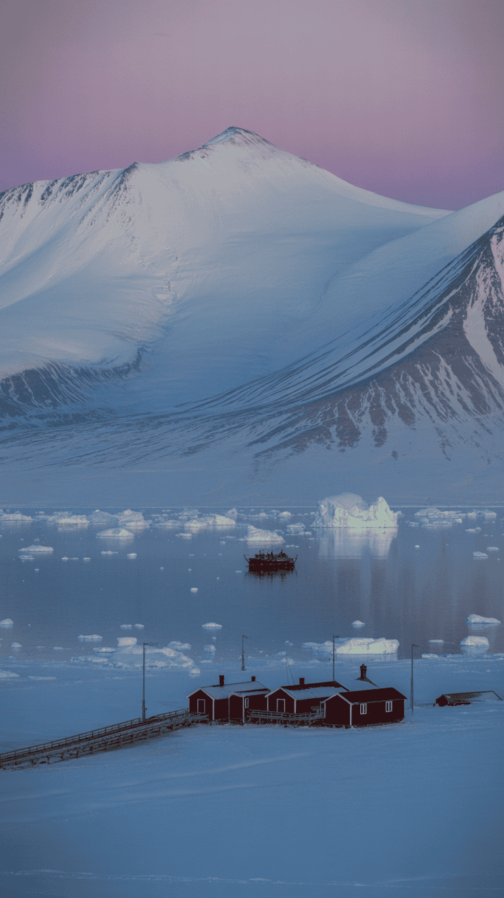 Red Arctic cabins overlooking icy waters with floating ice floes and a glacier backdrop in Svalbard at twilight.