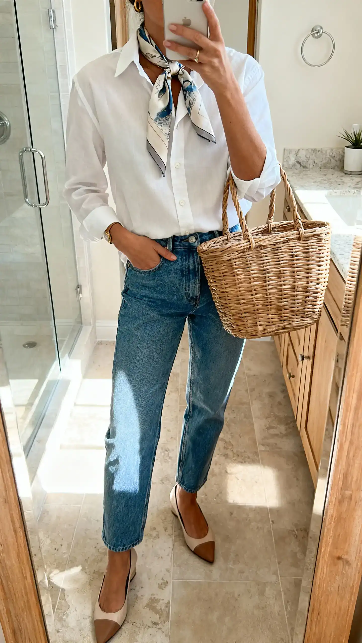 iPhone mirror selfie of a woman in a crisp white button-up shirt with blue denim and a silk scarf tied at the neck, paired with low heels and a basket tote, face not visible, bathroom mirror, bright morning light, iPhone photo quality.
