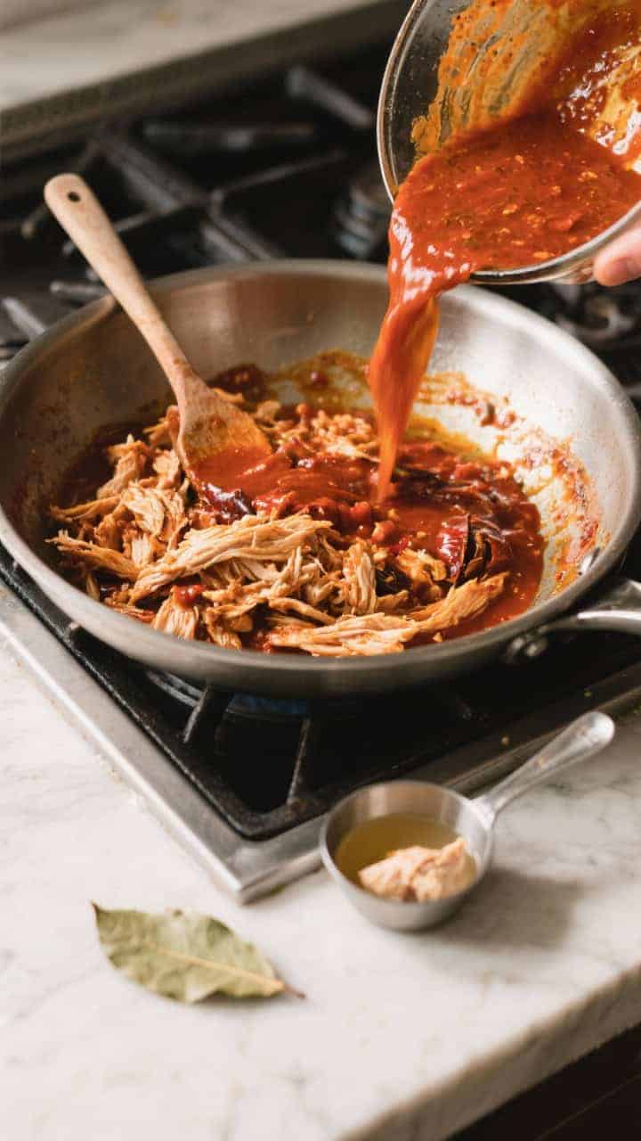 Cooking process: Overhead shot of the blended tinga sauce being poured back into a wide sauté pan a