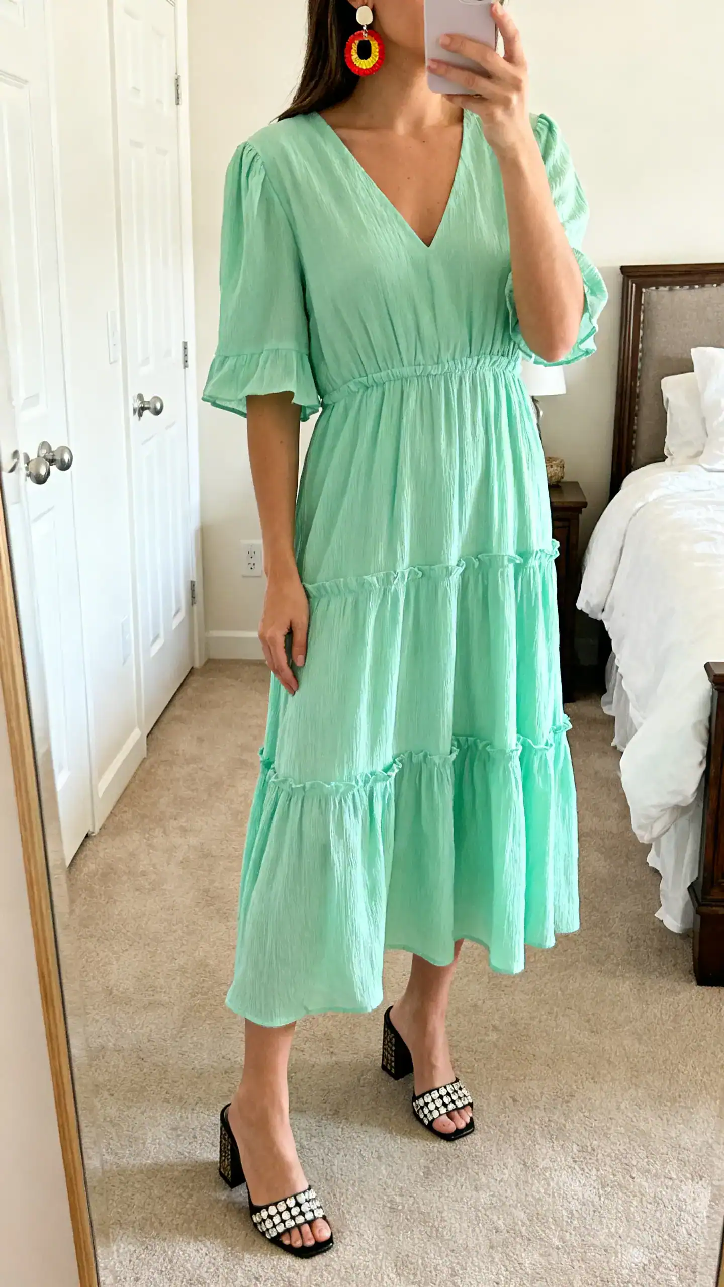 iPhone mirror selfie of a woman in a pistachio tiered dress with statement block-heel mules and bold earrings, face not visible, cropped at neck, bedroom mirror, gentle morning light, iPhone photo quality