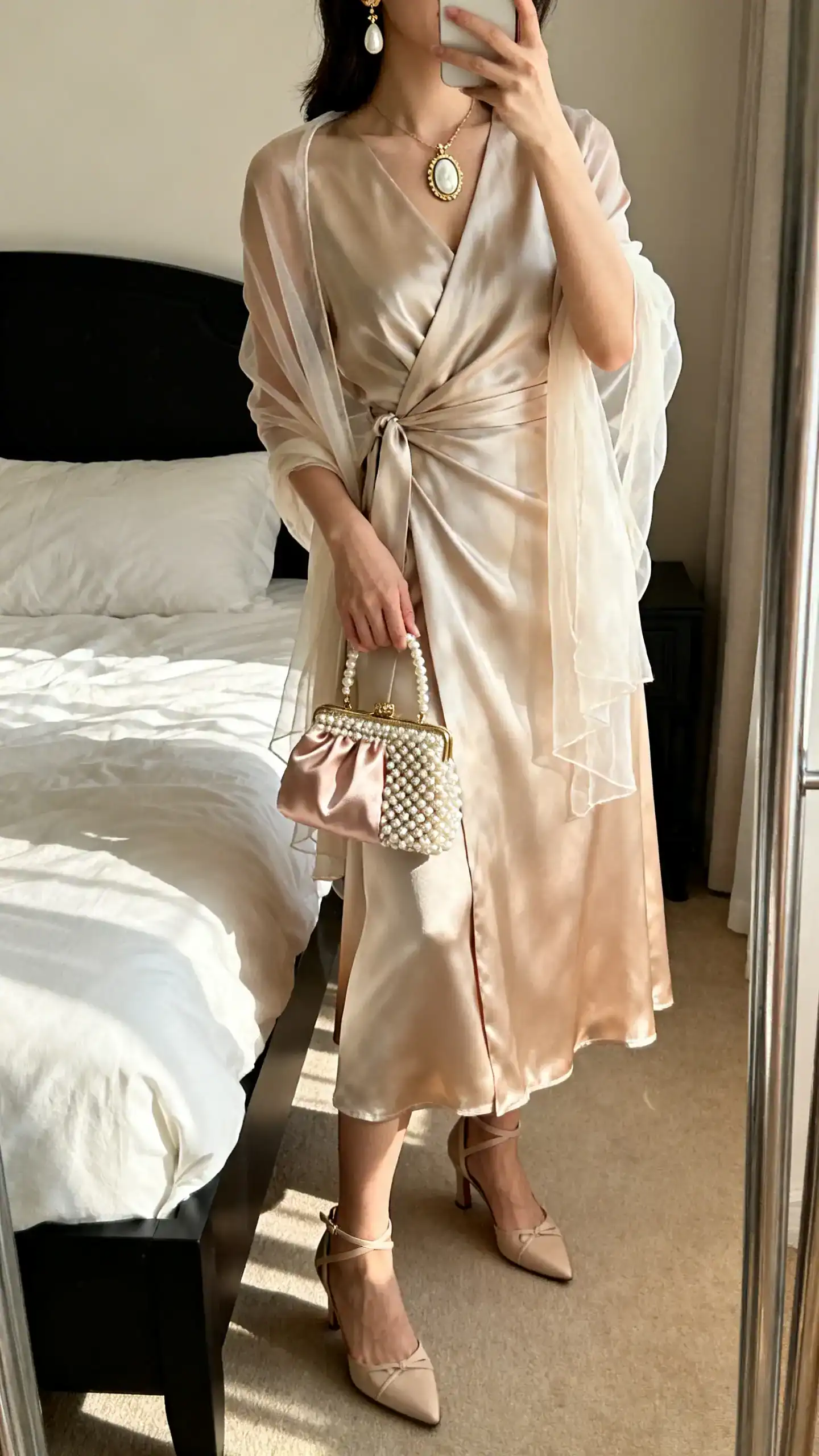 iPhone mirror selfie of a woman in a silk or silk-blend wrap dress (midaxi or midi), low ankle-strap heels or classic pumps, vintage-inspired drop earrings or a cameo-style pendant, a beaded or satin evening bag, and a sheer shawl; face not visible, cropped at shoulders, bedroom mirror, gentle morning light, iPhone photo quality.