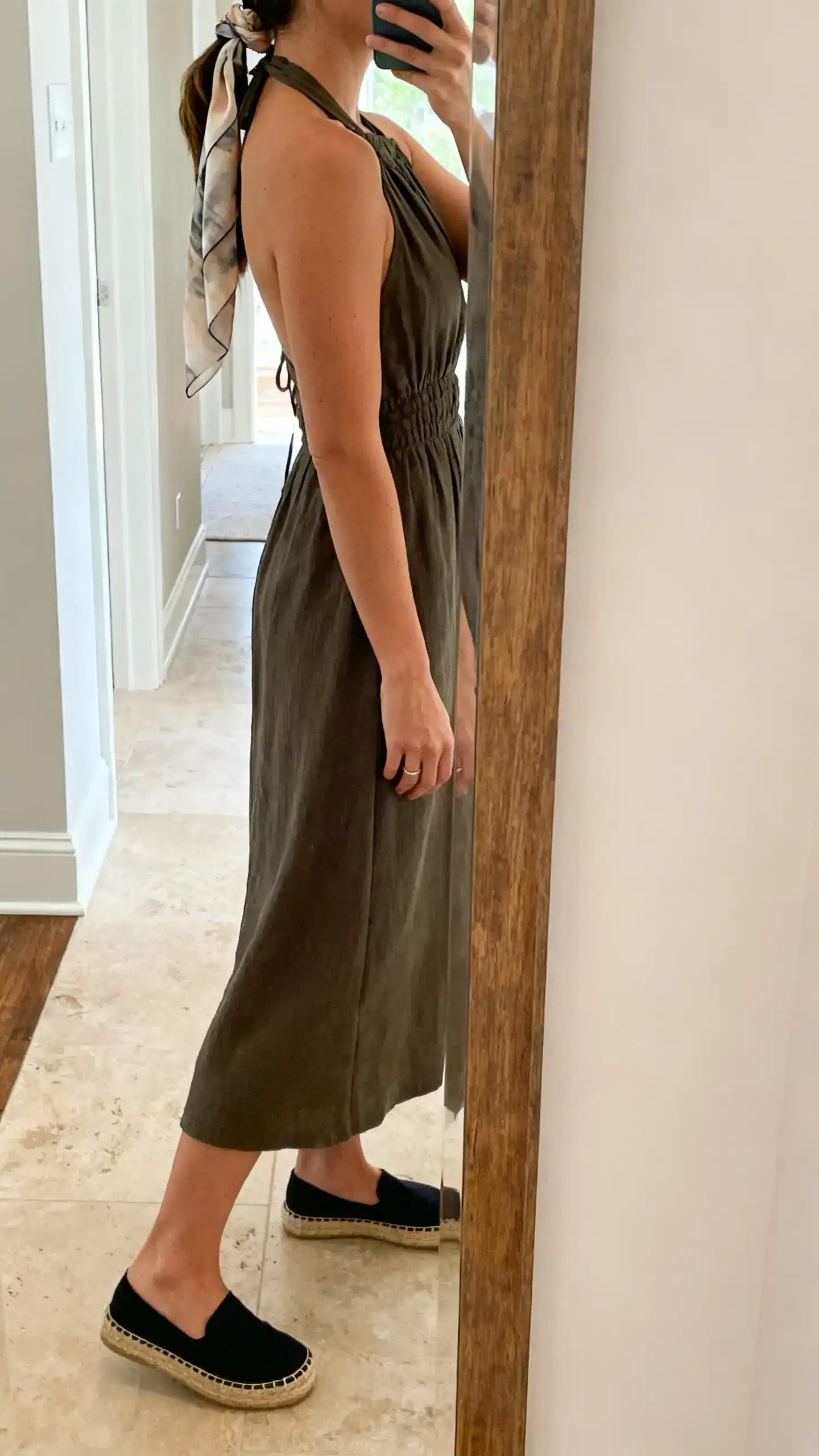 iPhone side-angle mirror selfie of a woman in a halter midi dress with classic espadrilles and a silk scarf tied in her hair, face not visible, entryway mirror, gentle morning light, iPhone photo quality