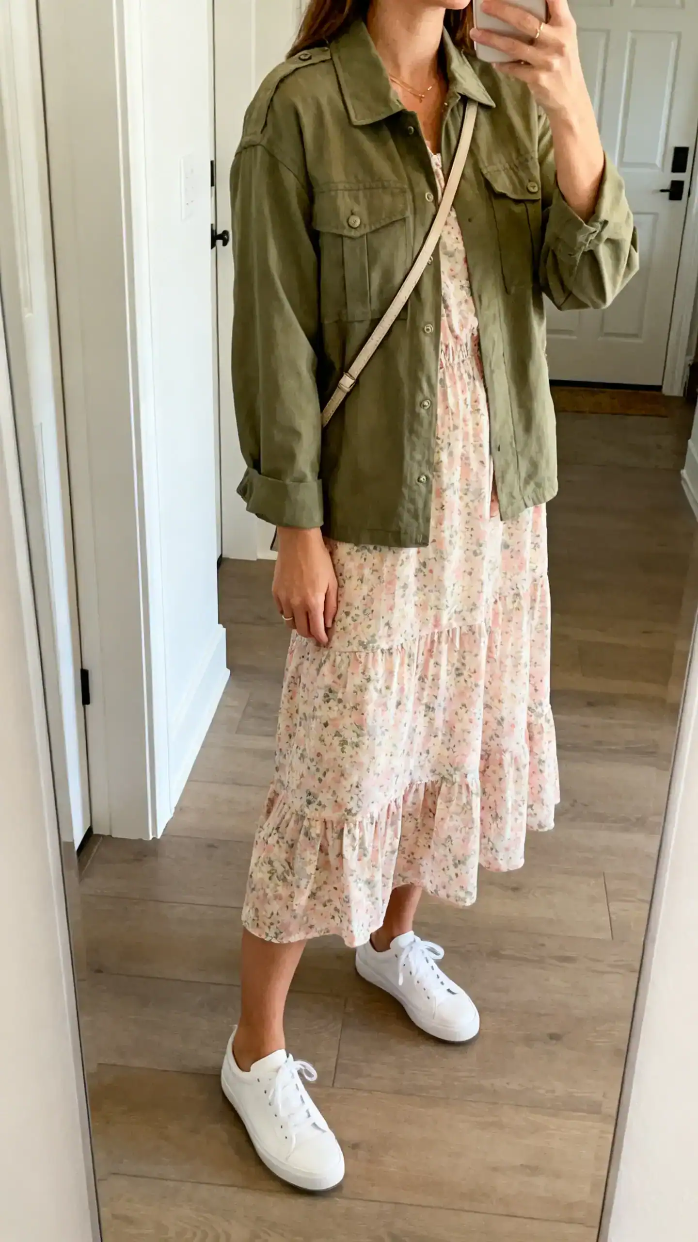 iPhone side-angle mirror selfie of a woman wearing a pastel floral dress with an olive utility jacket, white low-top sneakers and a crossbody, face not visible, entryway mirror, natural light, iPhone photo quality