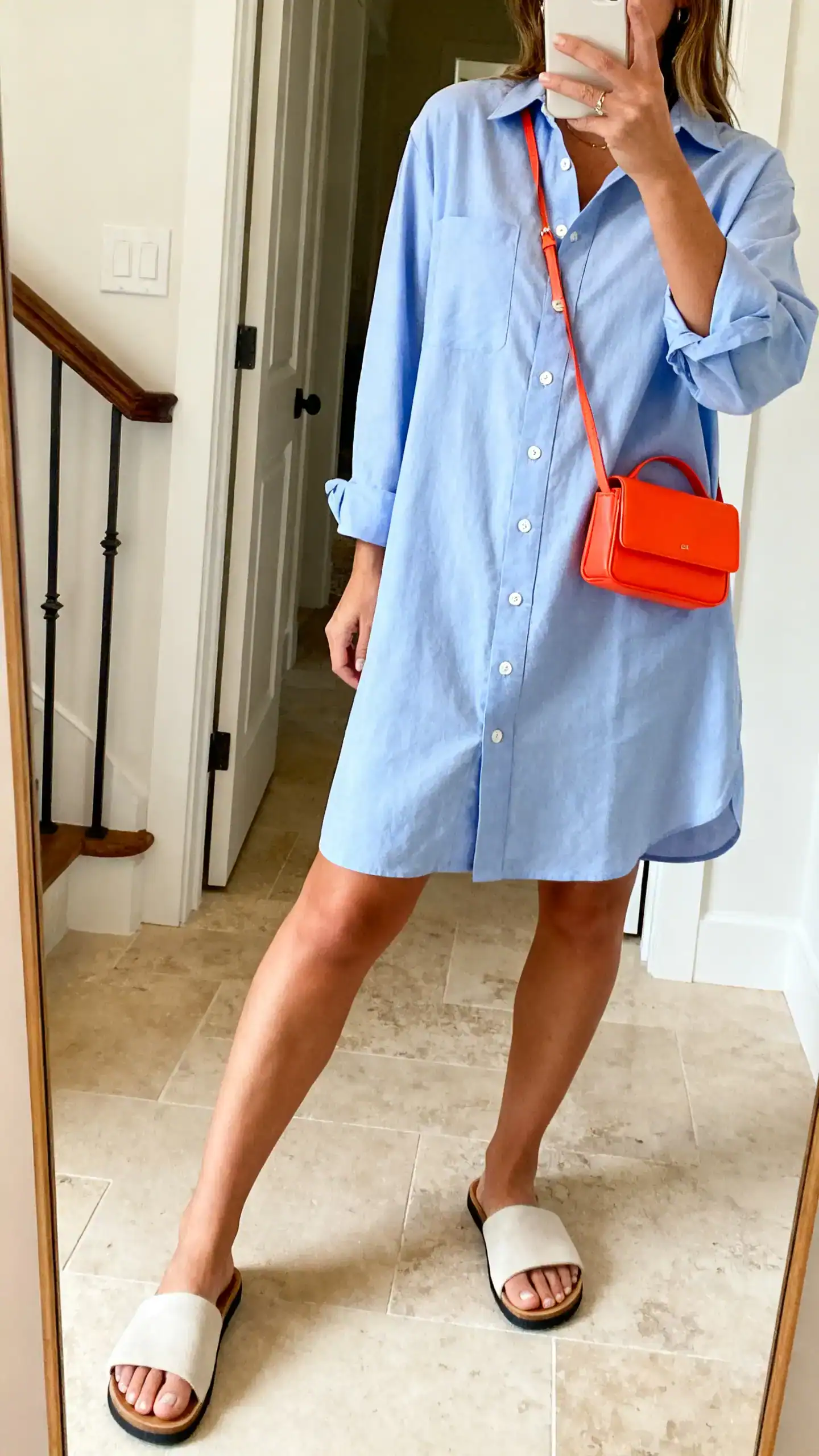 iPhone side-angle mirror selfie of a woman wearing a button-front shirt dress with simple slide sandals and a pop-of-color mini bag, face not visible, entryway mirror, morning natural light, iPhone photo quality