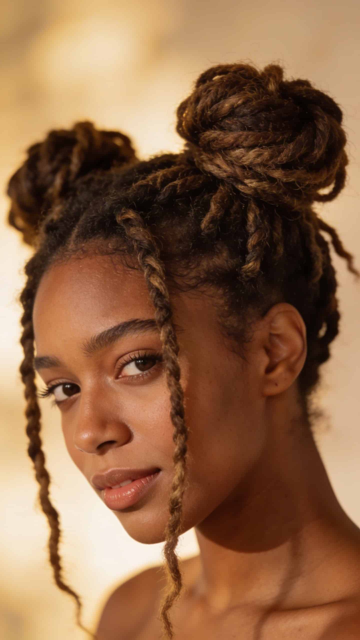 Black woman wearing locs styled in space buns with soft natural lighting