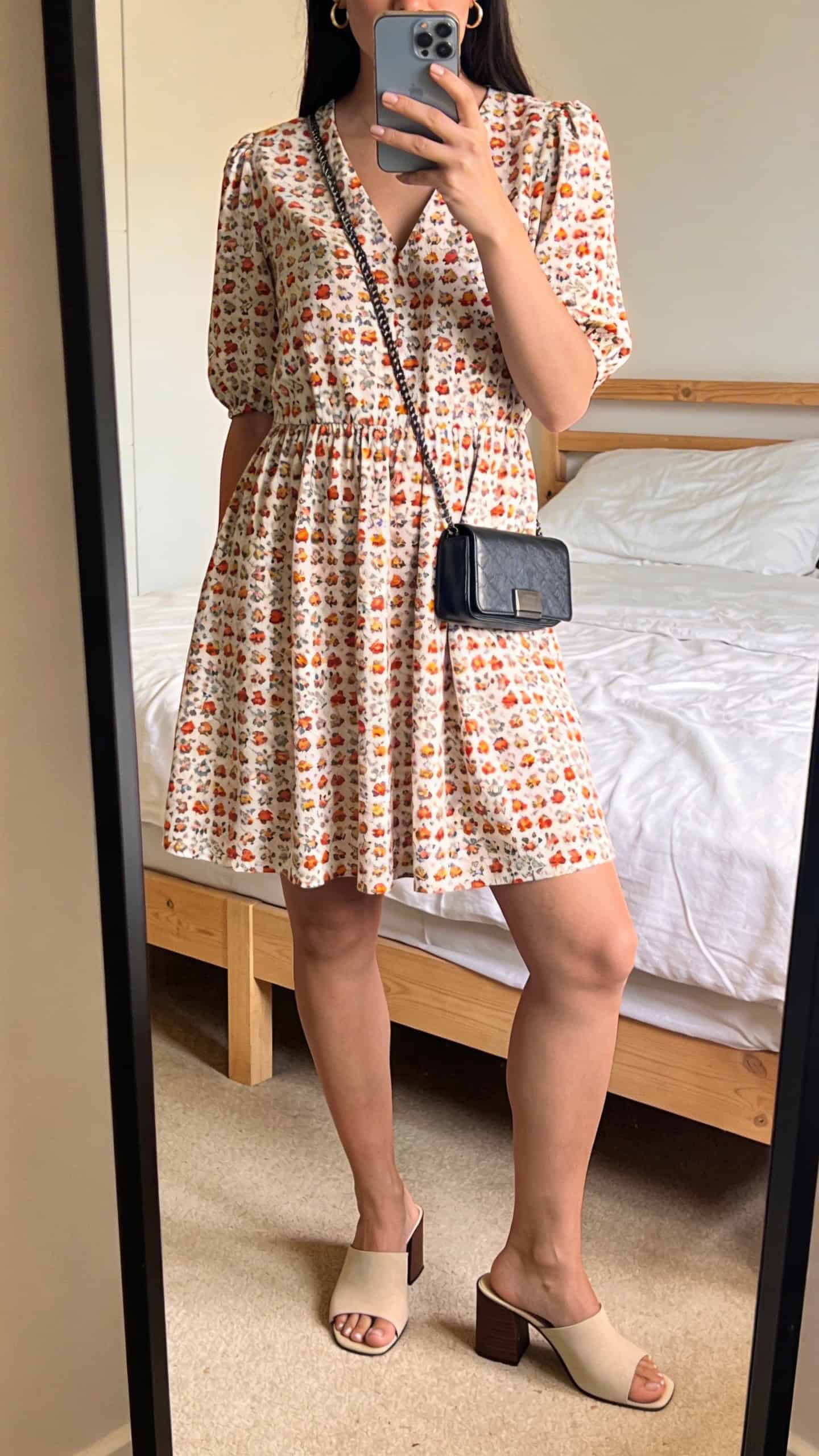 iPhone mirror selfie of a woman in a printed day dress (playful print, modest cut), block-heel mules, small hoop earrings, and a compact crossbody, face not visible, cropped at shoulders, bedroom mirror, bright natural light, iPhone photo quality