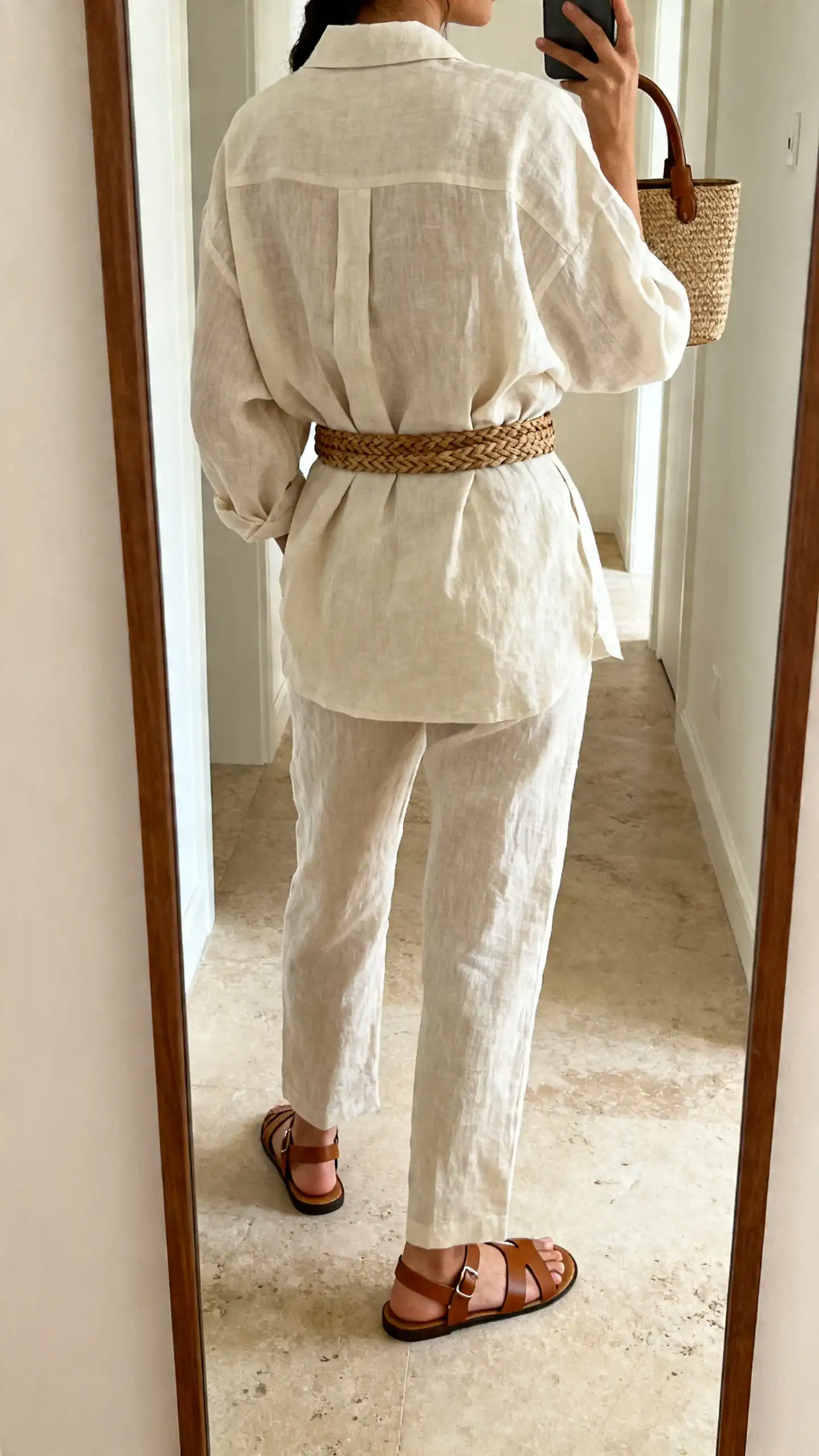 iPhone back-view mirror selfie of a woman in a monochrome linen set (boxy shirt and matching trousers), leather thong sandals, woven belt, top-handle bag, face not visible, hallway full-length mirror, natural daylight, iPhone photo quality