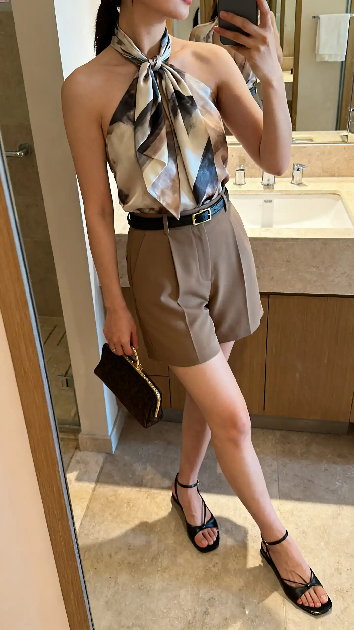 iPhone bathroom mirror selfie of a woman in a silk scarf top tied halter-style with tailored shorts, slim belt, small clutch, and low kitten sandals, face not visible, side angle, indoor lighting, iPhone photo quality