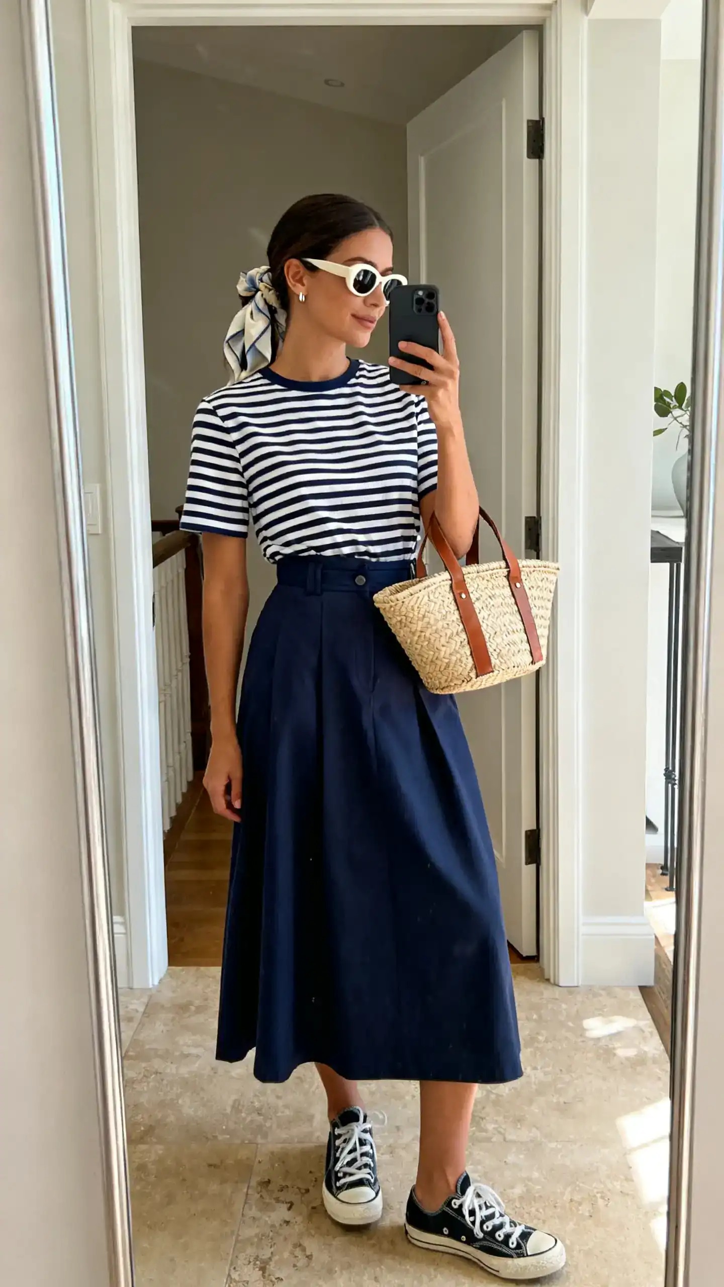 iPhone mirror selfie of a woman in a navy-and-white Breton striped tee tucked into a high-waisted cotton A-line midi skirt, canvas sneakers, basket bag with leather straps, retro sunglasses and a silk hair scarf, minimal stud earrings, face not visible, entryway mirror, natural morning light, iPhone photo quality.