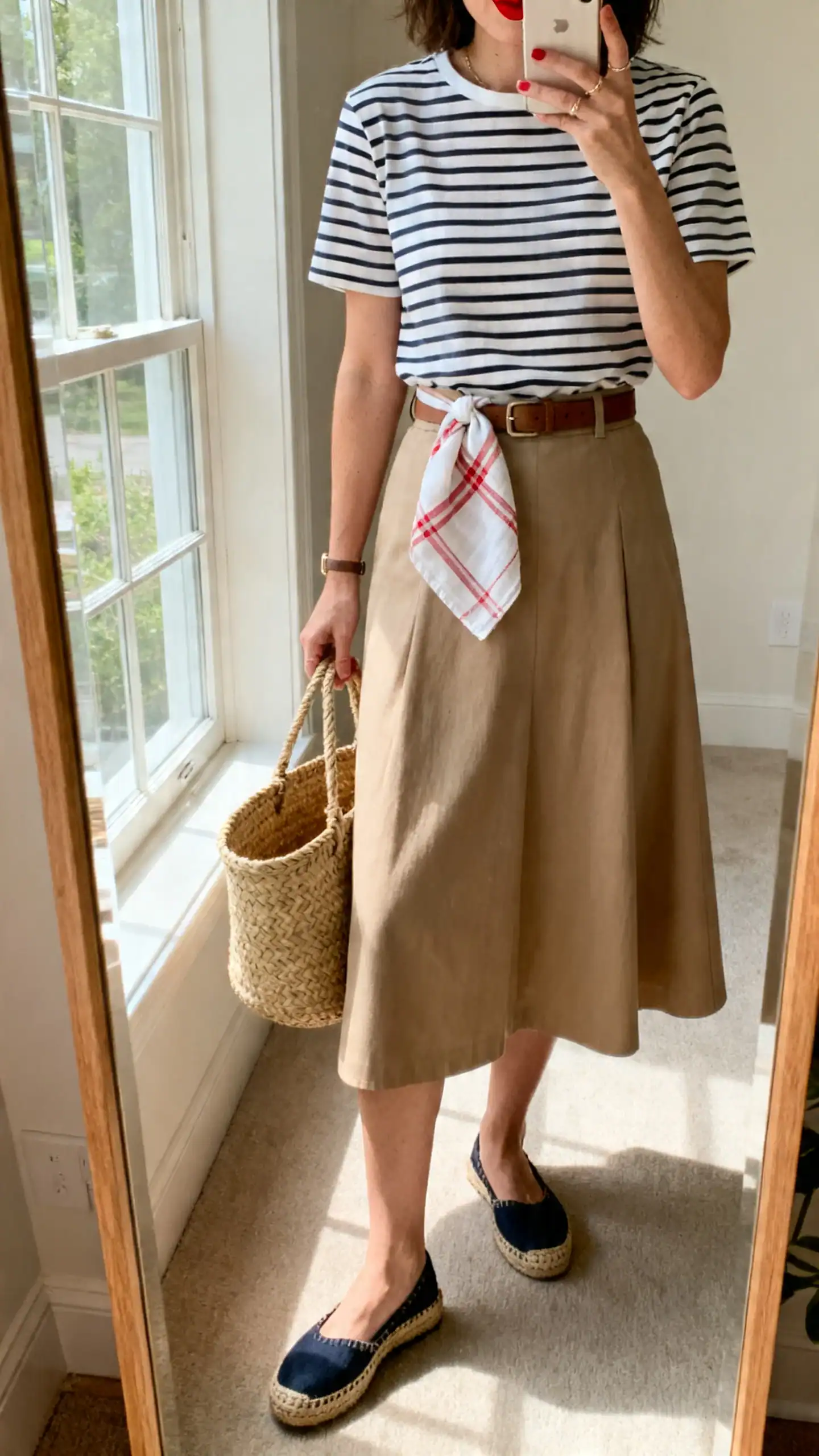 iPhone mirror selfie of a woman wearing a Breton stripe tee tucked into an A-line skirt, espadrille flats, basket tote, red lip seen on handkerchief only, face not visible, full-length mirror, daylight from window, iPhone photo quality