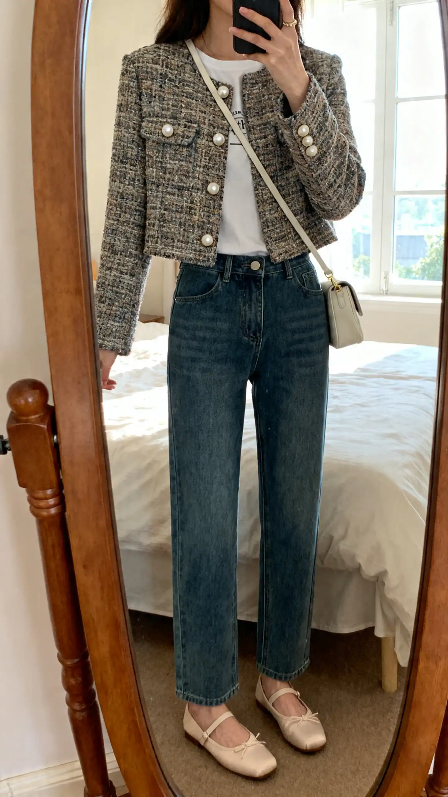 iPhone mirror selfie of a woman wearing a cropped tweed jacket over a simple tee with straight-leg denim, ballet flats, pearl studs, small shoulder bag, face not visible, bedroom mirror, natural window light, iPhone photo quality