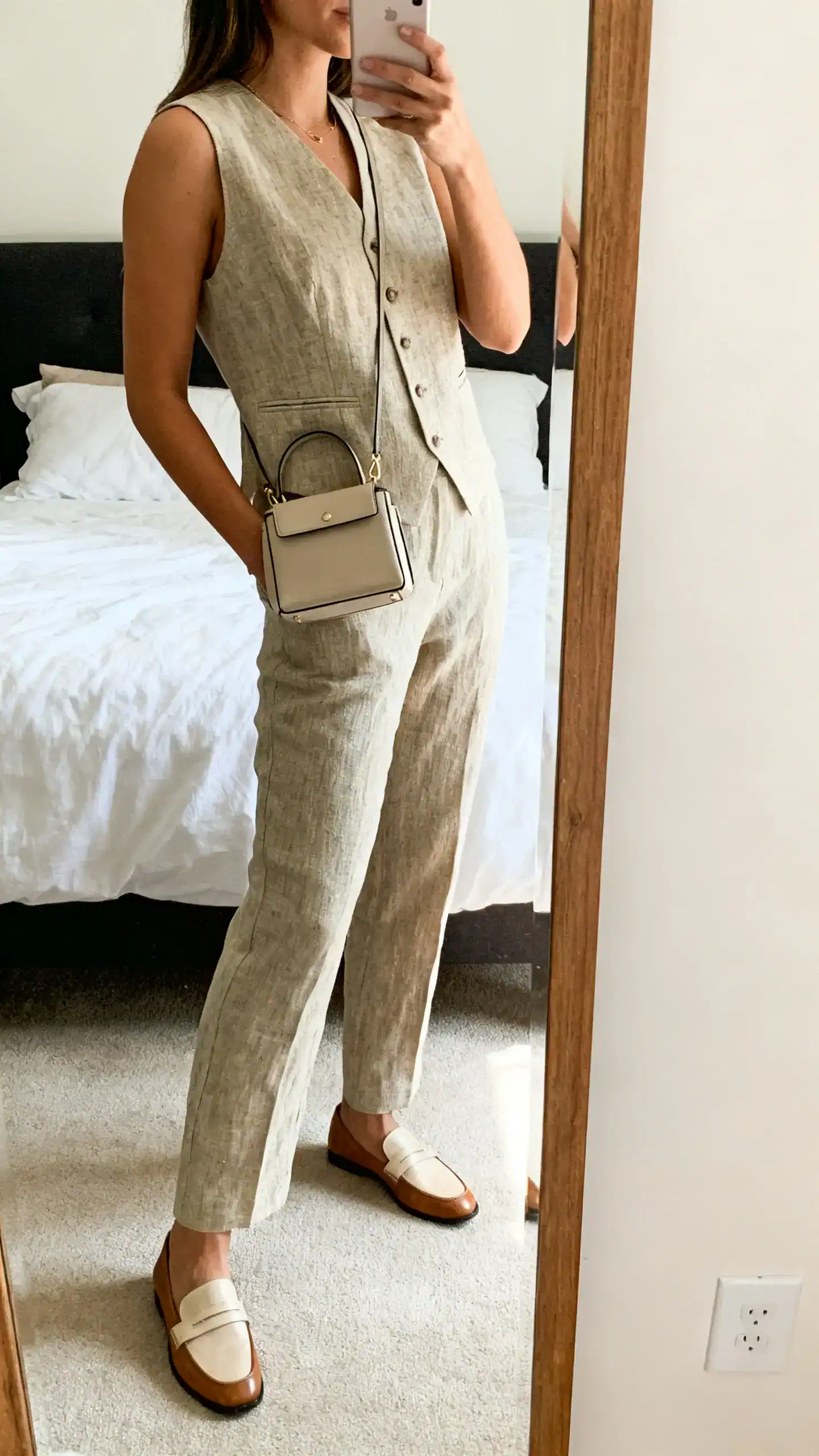 iPhone side-angle mirror selfie of a woman in a linen vest suit set (tailored vest + matching trousers) with loafers and a structured mini bag, face not visible, bedroom mirror, natural daylight, iPhone photo quality