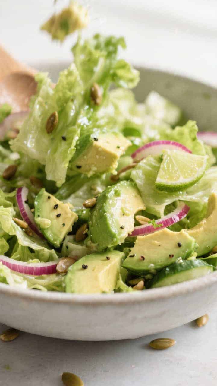 Close-up detail: Tossed Avocado Lime Lettuce Salad mid-toss in a large bowl, glistening lime vinaigr