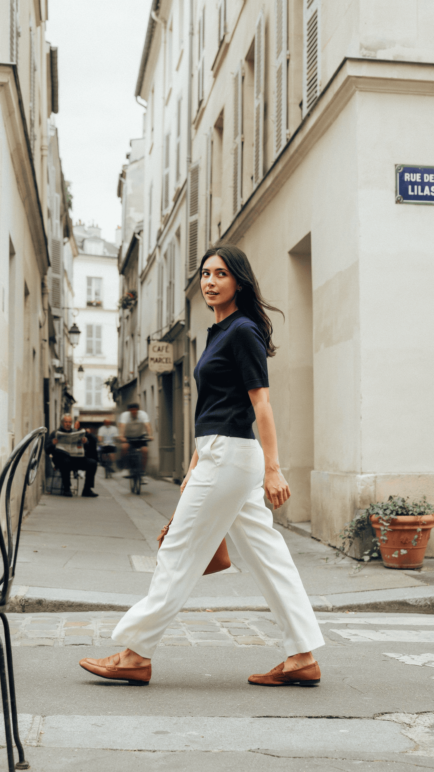 Woman wearing a fitted navy knit polo with flowing white trousers and leather loafers.