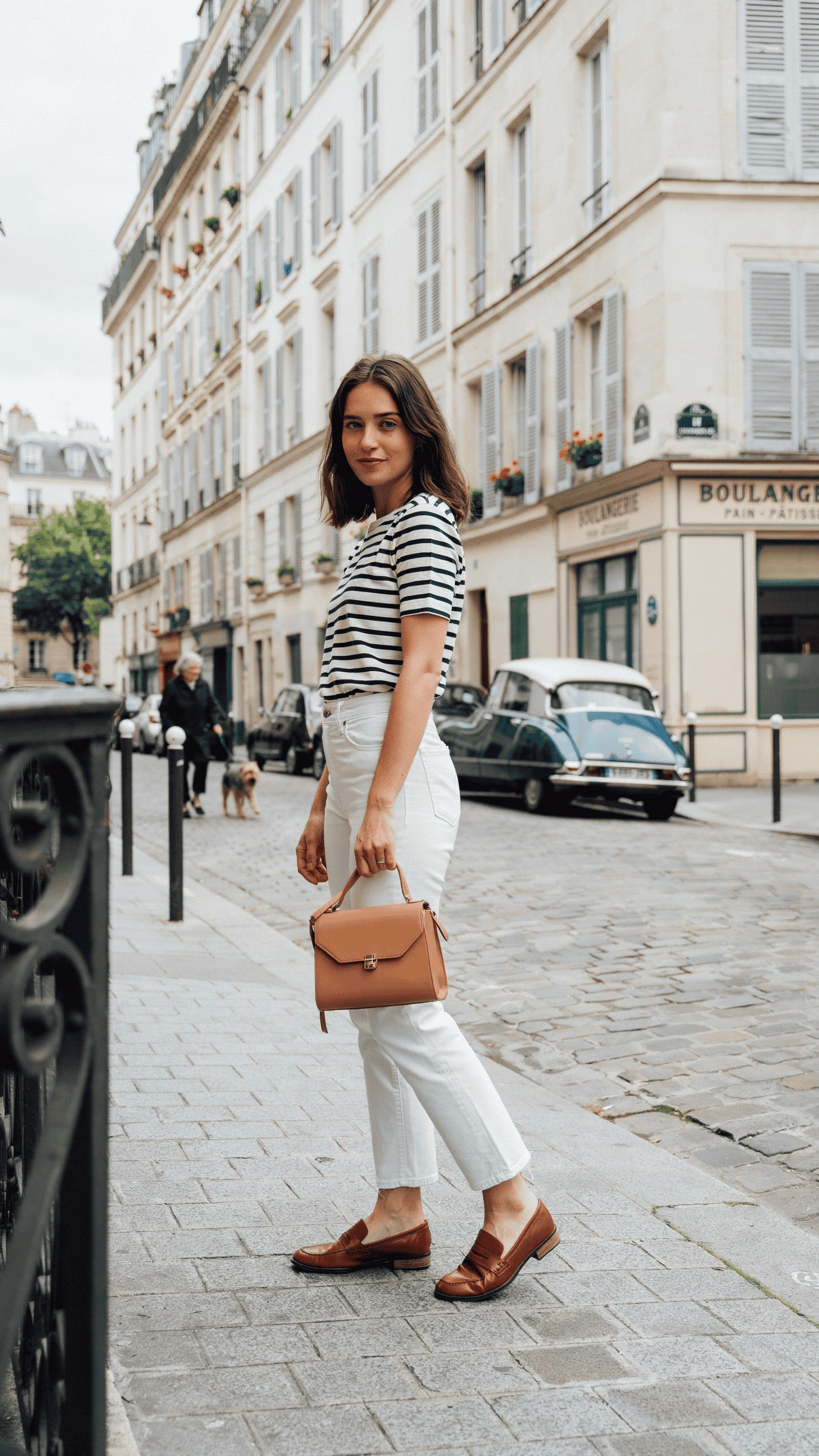 Breton striped top paired with white straight-leg jeans, loafers, and a tan leather handbag.