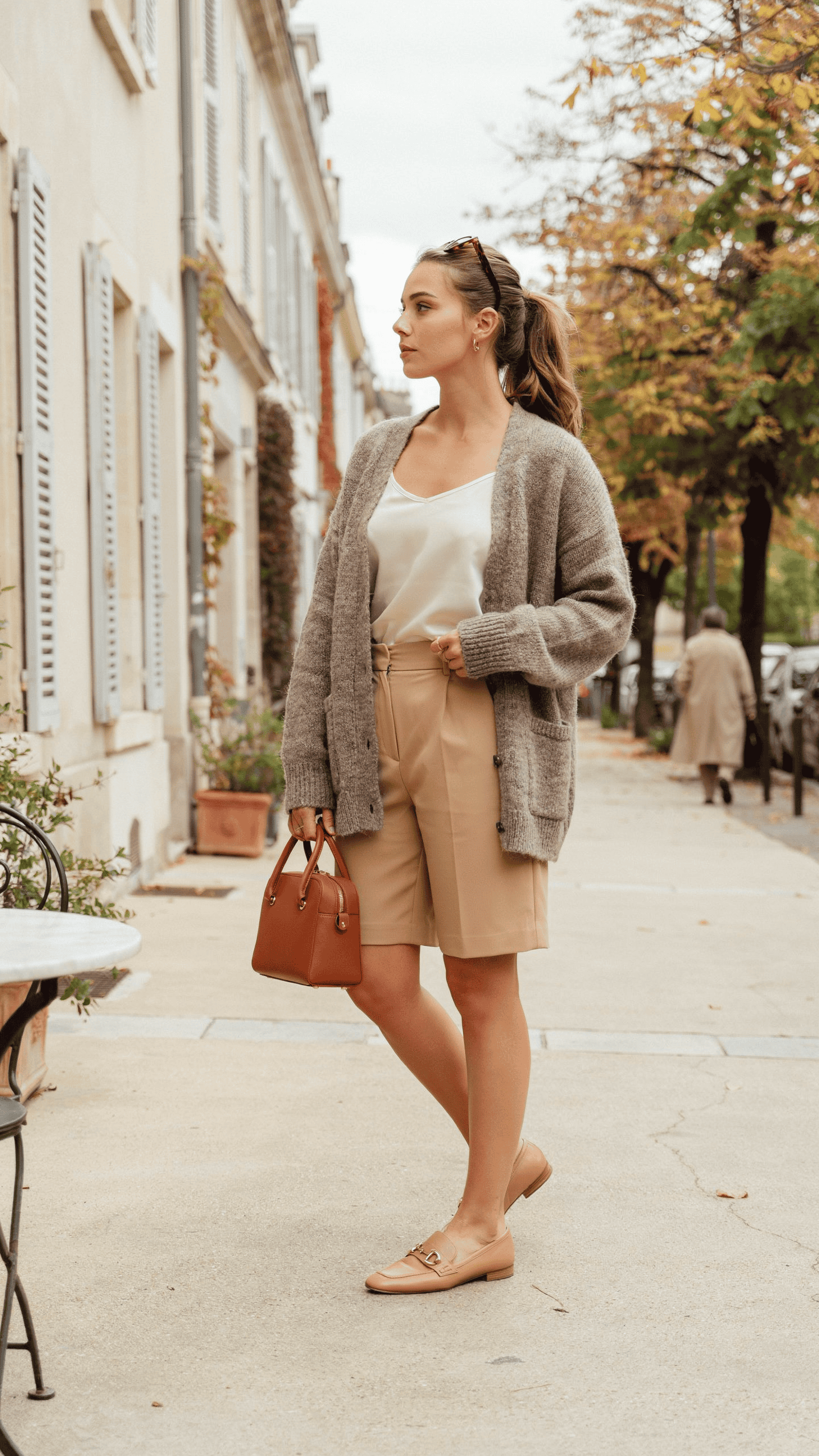 Grey cashmere cardigan styled with tailored Bermuda shorts, loafers, and a structured handbag.