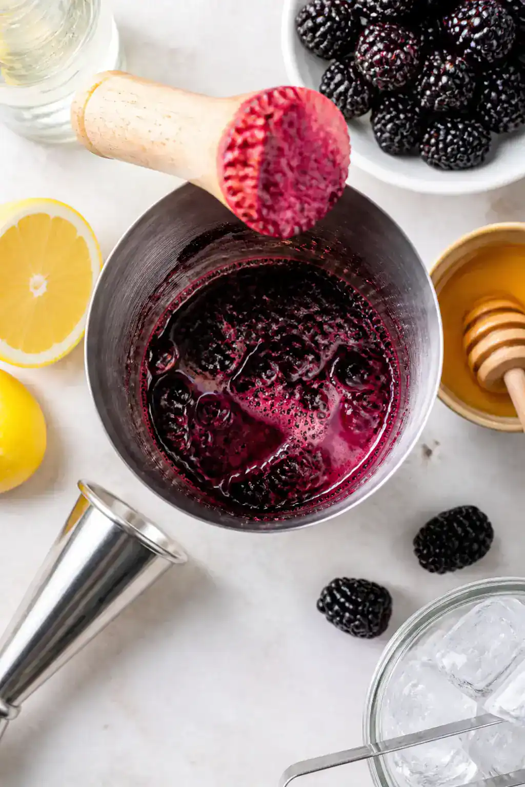 Cooking process: Overhead shot of the muddling stage inside a stainless shaker—smashed blackberrie