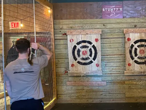 A person is about to throw an axe at a target in an indoor place that highlights the skilled work of Mid State Baths, known for shower refinishing in Carlisle.