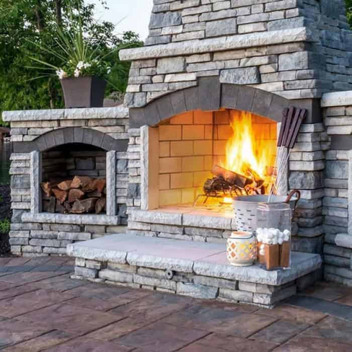 Outdoor stone fireplace with warm fire and decorative accessories.