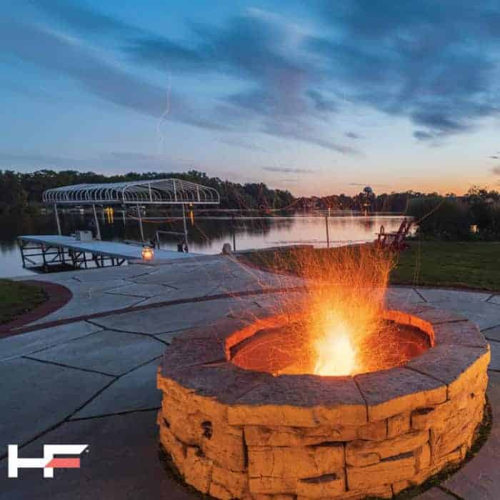 Outdoor fire pit with glowing flames by the lake at dusk.