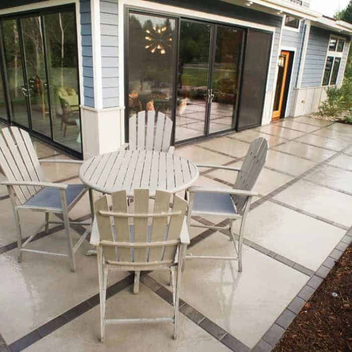 Outdoor patio with round table and chairs in front of a modern house.