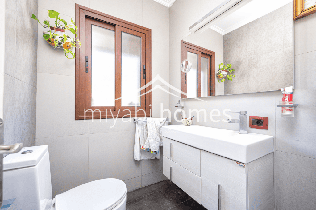 Modernes Badezimmer mit Fenster, Waschbecken und Pflanzen.