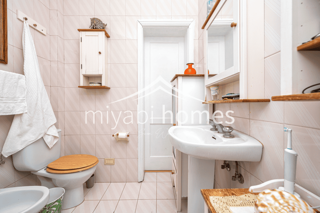 Kleines Badezimmer mit weißen Fliesen, Waschbecken und WC in einer Ferienwohnung.