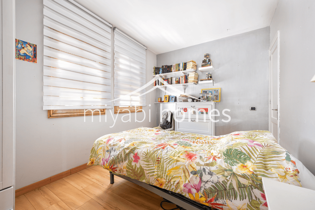 Gemütliches Schlafzimmer mit buntem Blumenbett und Bücherregal.
