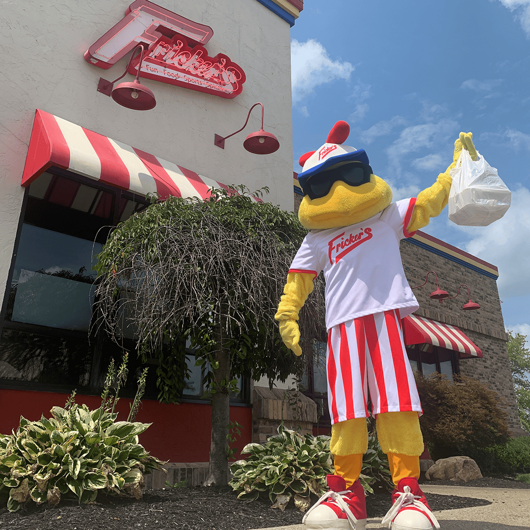 Fricker's chicken mascot holding a bag of carryout food in front of a Fricker's location.