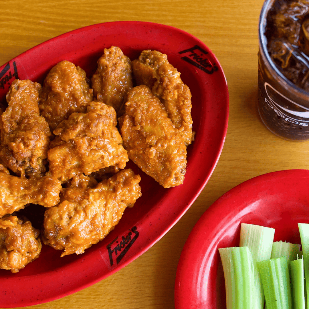 A close up shot of Fricker's chicken wings with celery and a soda.