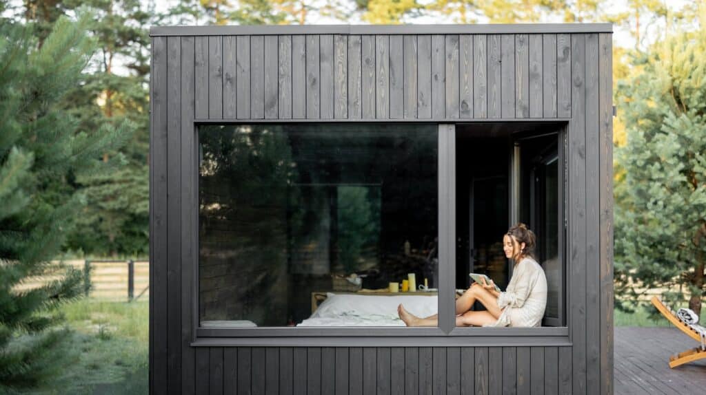 Mujer leyendo en cabaña moderna rodeada de naturaleza.