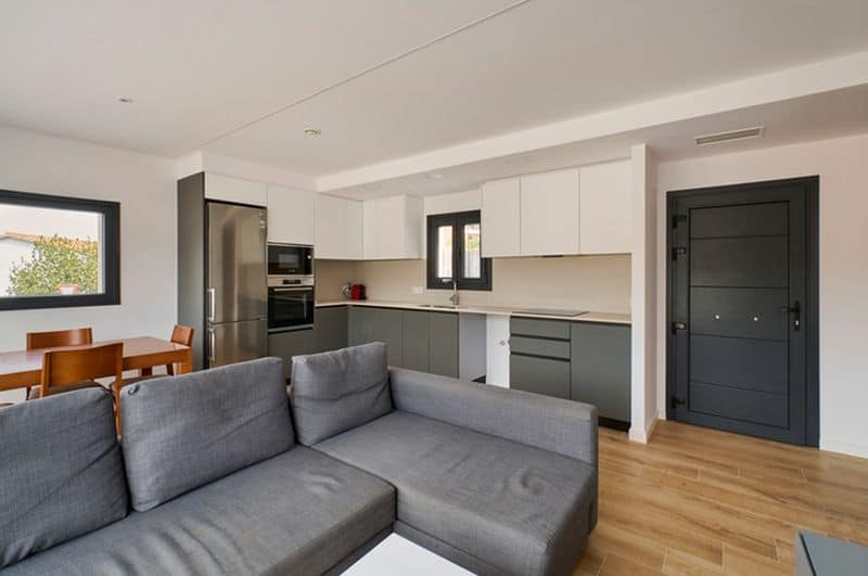 Salón moderno con cocina integrada y sofá gris.