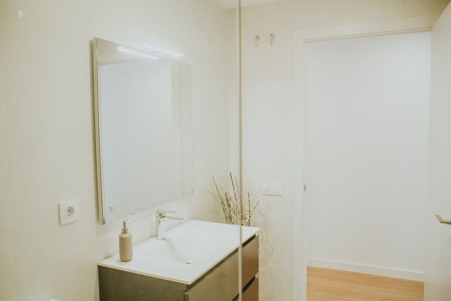 Baño moderno con espejo grande y pared blanca.