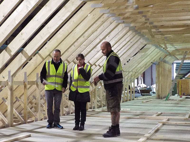 Three workers inspecting a wooden roof structure under construction.
