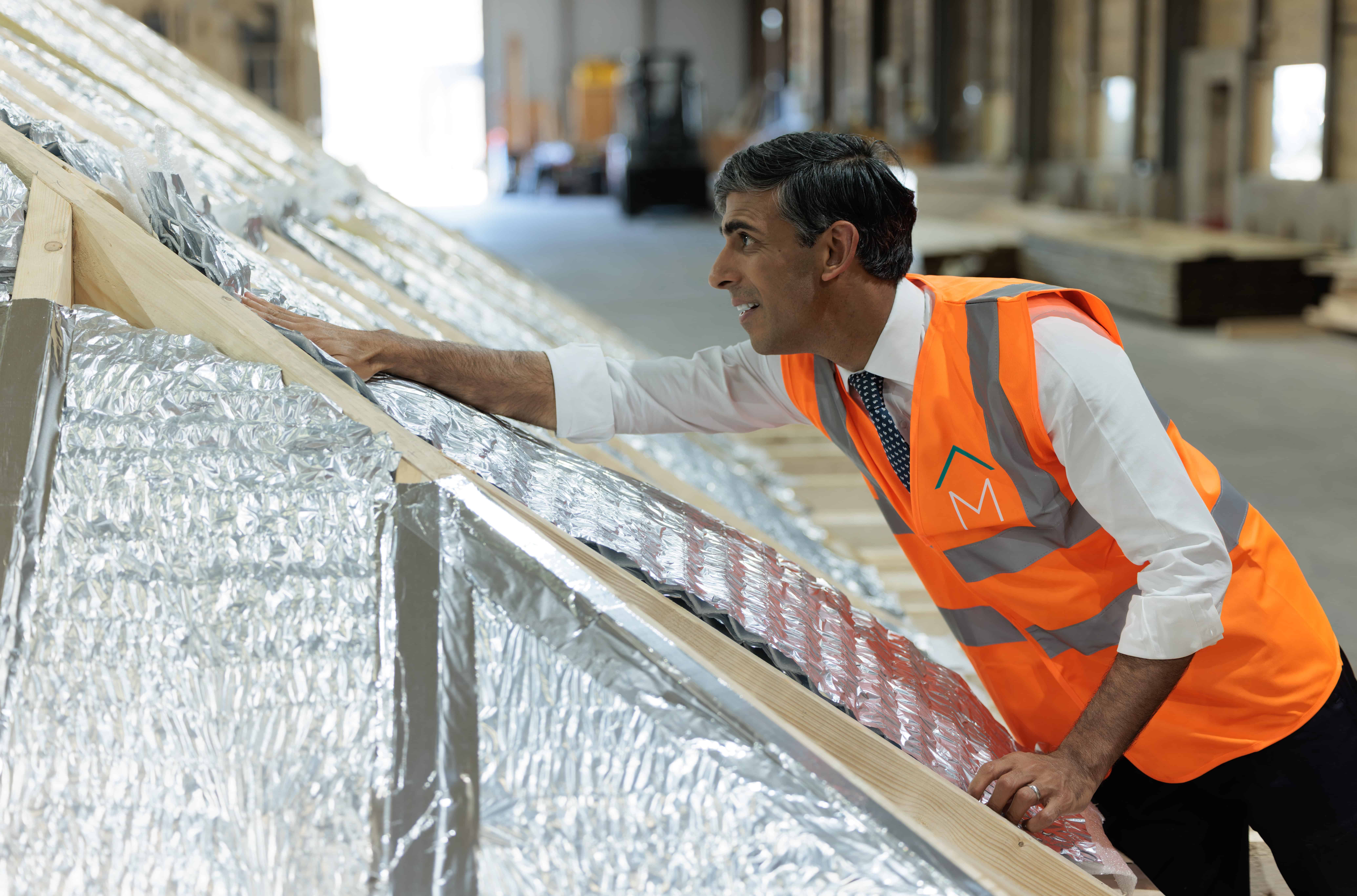 Man in safety vest inspecting modular construction panels in warehouse.