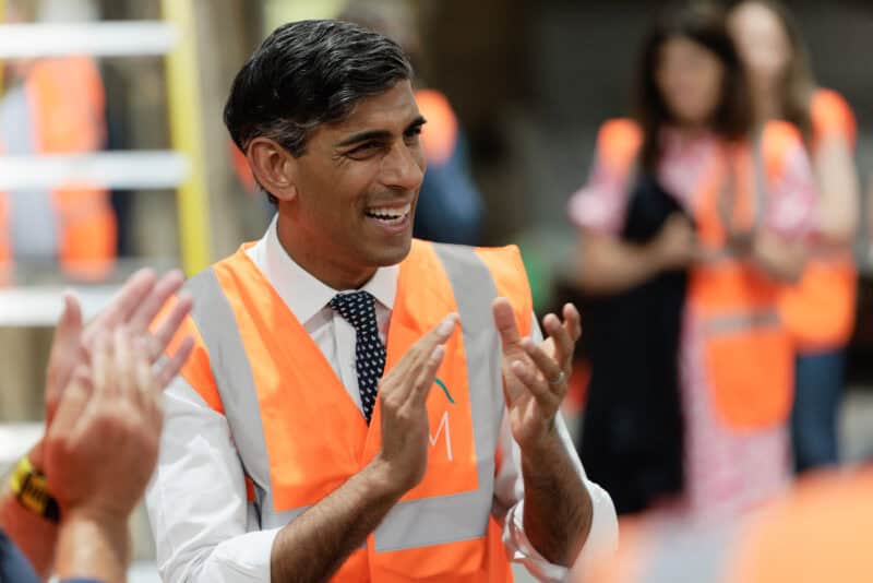 Rishi Sunak at a construction site wearing a high-visibility vest and smiling.