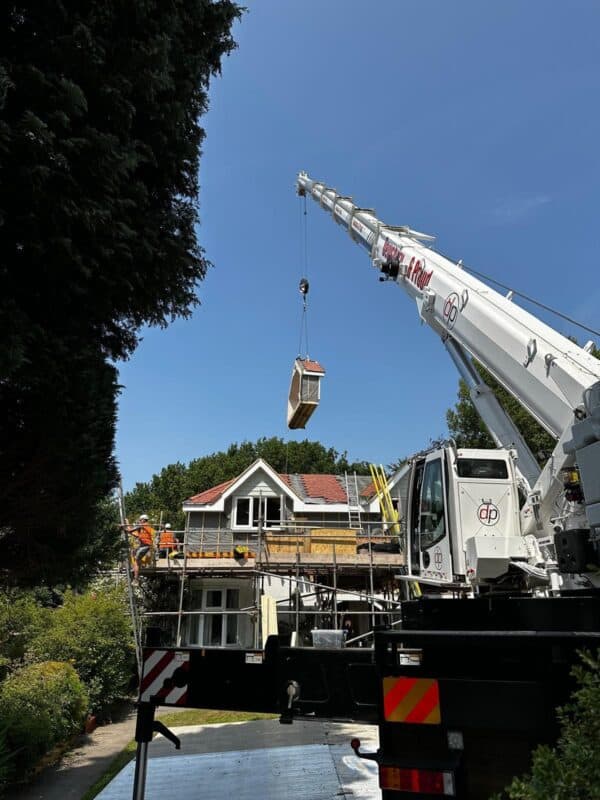 Crane lifting a house section during off-site loft conversion process.