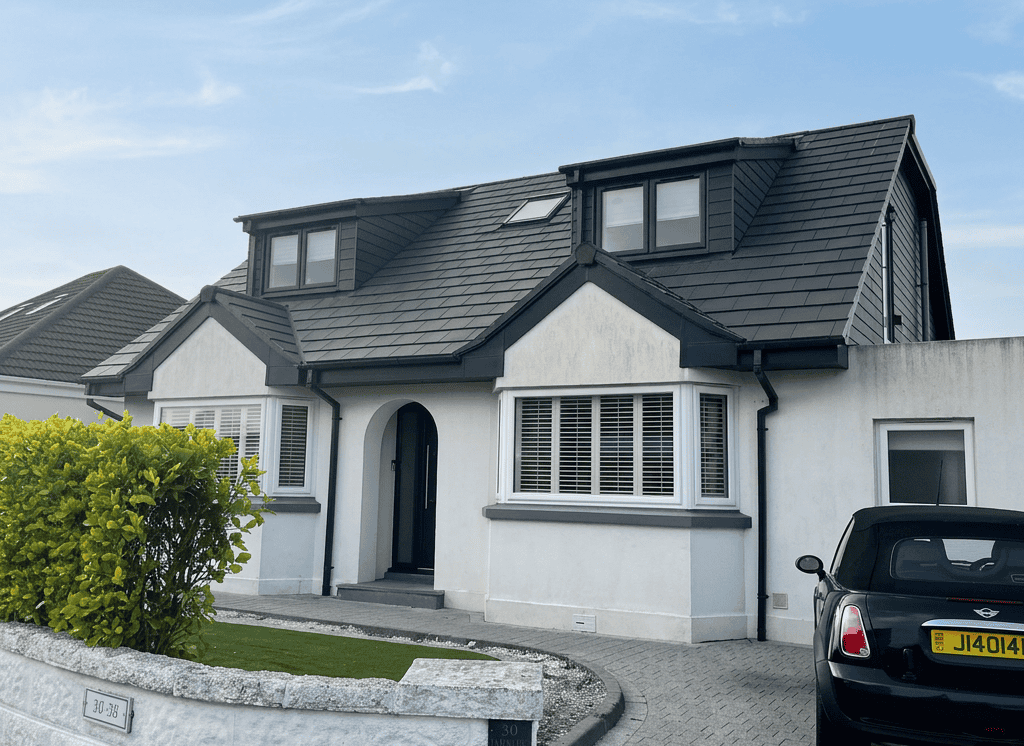 Modern white house with black roof and dormer windows, driveway, and garden.
